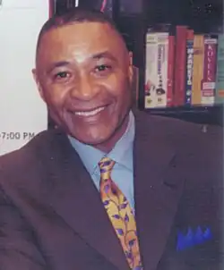 Man wearing a suit with a blue shirt. He has a crew-cut haircut.