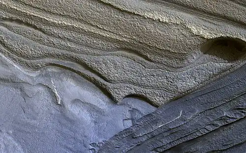 Image 11 Climate of Mars Photograph credit: NASA / JPL–Caltech / University of Arizona Although Mars is smaller than the Earth and 50 percent farther from the Sun, its climate has important similarities with the Earth, such as the presence of polar ice caps, seasonal changes and observable weather patterns. This image shows layered deposits in Planum Boreum, in the north polar region of Mars, which formed from a 3-kilometre-thick (2 mi) stack of dusty water-ice layers about 1,000 km (600 mi) across. The layers record information about the climate of the planet stretching back several million years. Erosion has created scarps and troughs that expose the layering. The tan-colored layers are the dusty water ice of the polar layered deposits, however a section of bluish layers is visible below them. These bluish layers contain sand-sized rock fragments that likely formed a large polar dunefield before the overlying dusty ice was deposited. This photograph, depicting an area approximately 1.3 km (0.8 mi) across, was captured by the HiRISE camera on board NASA's Mars Reconnaissance Orbiter. More selected pictures