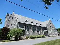 A two-story gray masonry church with a square turret.