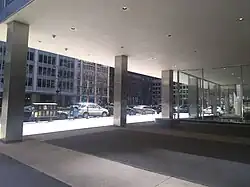 View of the ground-floor privately owned public space under Lever House's base. The space includes a grid of floor tiles. The second floor of the building is held up by steel columns. Park Avenue is visible in the background.