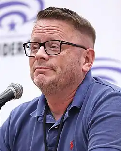 Patrick Ness sitting in front of a microphone