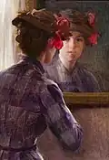 Oil painting of a woman in a high necked, long sleeved dress looking at herself in the mirror. Her hair is in a bun and she wears a brown hat with red flowers on the right side.