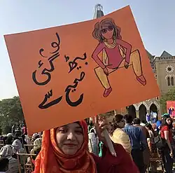 A woman proudly holds a sign with a picture of a woman sitting with her legs apart.