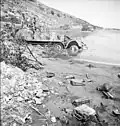 A beach near Porto Farina strewn with debris - a German SdKfz 11 half-track gun tractor lays in the water