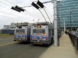 Two silver-painted trolleybuses at a bus stop. Rewiring pans are visible on the overhead lines.