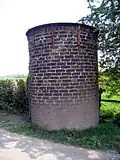 A cylindrical brick structure standing by a footpath.