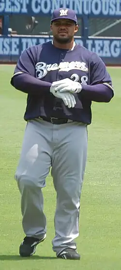 A man wearing a navy blue Brewers jersey, gray pants, and a navy blue cap adjusts his white batting gloves