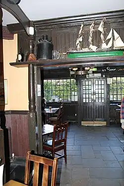 A dark, traditional interior of a pub with wooden beams, a tiled floor, and small model ships.