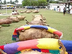 A katoaga with donated pigs in front of the royal palace (right).