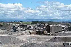 Quarry plant works, with piles of stone and green fields and hills beyond the quarry site