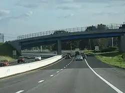 Ground-level view of a divided four-lane freeway; directly in front a large, curved bridge crosses over the freeway.