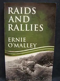 "Colour photograph of the front cover of Raids and Rallies by Ernie O'Malley, showing a picture of three hatted men armed with shotguns lying in ambush in a ditch"