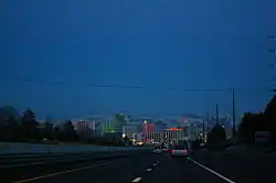 Dusk view of a freeway descending into a neon lit cityscape.