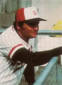 A man wearing a white baseball uniform and orange cap with a white Old English "D" font in the middle.
