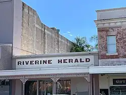 Riverine Herald sign across building between two taller buildings