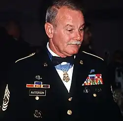 A gray-haired white man wearing a formal military uniform with a star-shaped medal hanging from a ribbon around his neck