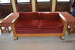 A replica of one of the house's sofas. The seats have red upholstery, and there are wooden desks on either side of the sofa.