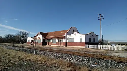 A building which is 195 feet (59 m) long and 26 feet (7.9 m) wide. The building architecture is eclectic, exhibiting both Spanish and Italian influences. The lower section of the exterior wall is brick, while there is covered with stucco. The stucco is painted white, decorated with tan painted trim. The center section has a gabled roof, with semicircular walls extending above the roof line on each end. The large window in the center is arched. Other windows have an arch design embedded in the stucco.