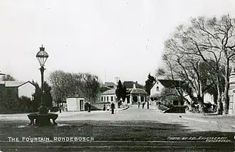 A street scene of Main Road Rondebosch, Cape Town around the turn of the 20th century. The recently installed Rondebosch Fountain can be seen to the left in the foreground.