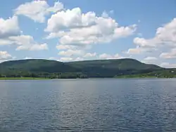 A lake with green mountains behind, under a cloud-filled blue sky