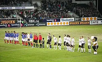 A line of footballers, in blue and white, respectively, at a large stadium