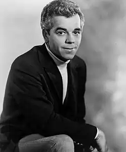 A fair-haired man wearing a dark jacket, smiling slightly