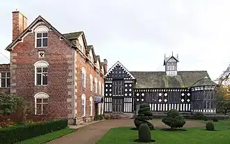 View of old country house seen across gardens; the exterior walls of the house are in Tudor black and white