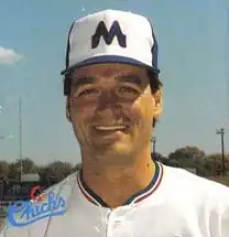 A man wearing a white baseball uniform and blue cap with a white "M".