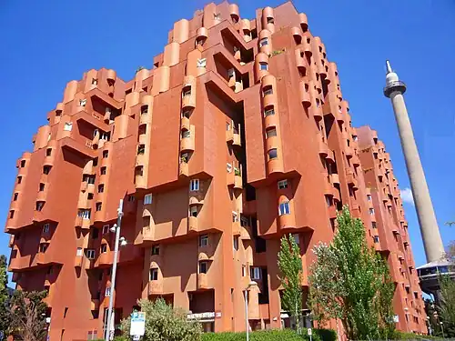 irregularly-shaped, multi-story red building with many small, round balconies