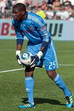 An African American male in a blue uniform is playing soccer.
