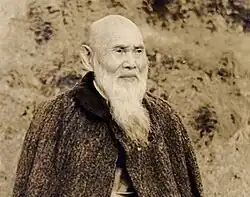 Black-and-white picture of Soda Kaichi, an elderly man with a shaved head and a long, white beard, wearing a dark gown.