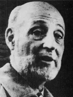 = A black-and-white image of a middle-aged bald man who is speaking