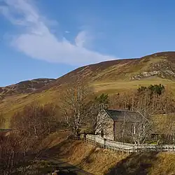 A stone church with a path beside it, and hills in the background.