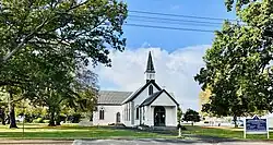 A photograph of a church with a tall spire in a grassy environment