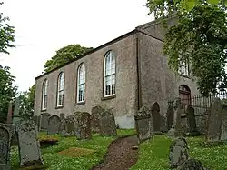 A plain chapel-like building with Georgian-style windows on a hill, surrounded by a dense churchyard.