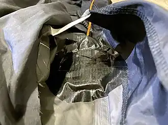 The inner taffeta lining cut open, exposing the outermost fabric from the inside. The squib device is then aligned to the weakened area and attached with duct tape.