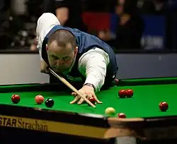 Stephen Maguire holds his cue and lines up a shot into a corner pocket.