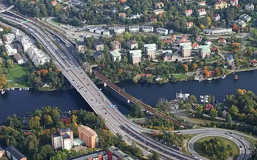 Stocksundet from southwest, with the motorway bridge and the present railway bridge in the centre of the image, and pylons for the old railway bridge and the old station building seen to the right. (September 2012)
