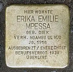 Brass plate inscribed in German "Hier wohnte Erika Emile Mpessa geb. Diek, verh. Ngambi ul Kuo, Jg. 1916. Ausgegrenzt/entrechtet. Berufsverbot 1939. Überlebt."