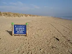 Sign on a beach, reading "National Trust: Naturists may be seen beyond this point"