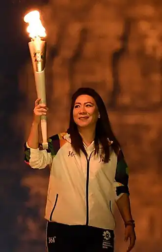 Susi Susanti, pictured from about the waist up, holding a torch in her right hand and looking up towards it at the 2018 Asian Games.