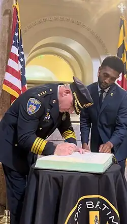 Worley bending over to sign a document as Brandon Scott watches from the side.