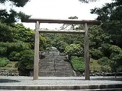 Stairs leading through a wooded area to a stone structure beyond a large torii.