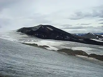 A black cone-shaped mountain rising over glacial ice in the foreground