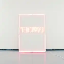 A photograph of a rectangular pink neon sign against a pale blue background, reading "The 1975".