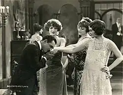 A man embraces the hands of three well-dressed women