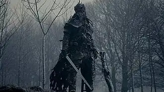 A tall armored man wielding a sword in a snowy landscape