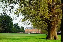 An oak tree on the right of the image, in the background is a large red-brick country house