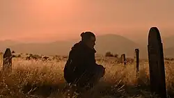 Ellie crouches at Joel's grave