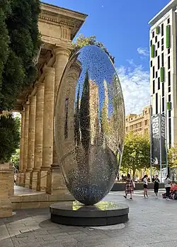 Tall egg-shaped monument made from stainless steel sheet, with thousands of perforations of various sizes.